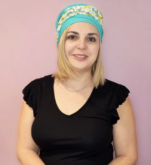 Femme souriante en intérieur sur fond rose pastel, portant bandana turquoise à motifs floraux et top noir à manches courtes avec col en V