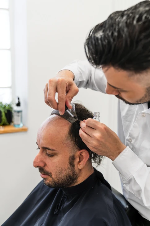 Intérieur de salon de coiffure, coiffeuse appliquant un traitement capillaire sur cheveux blonds mi-longs d'une cliente