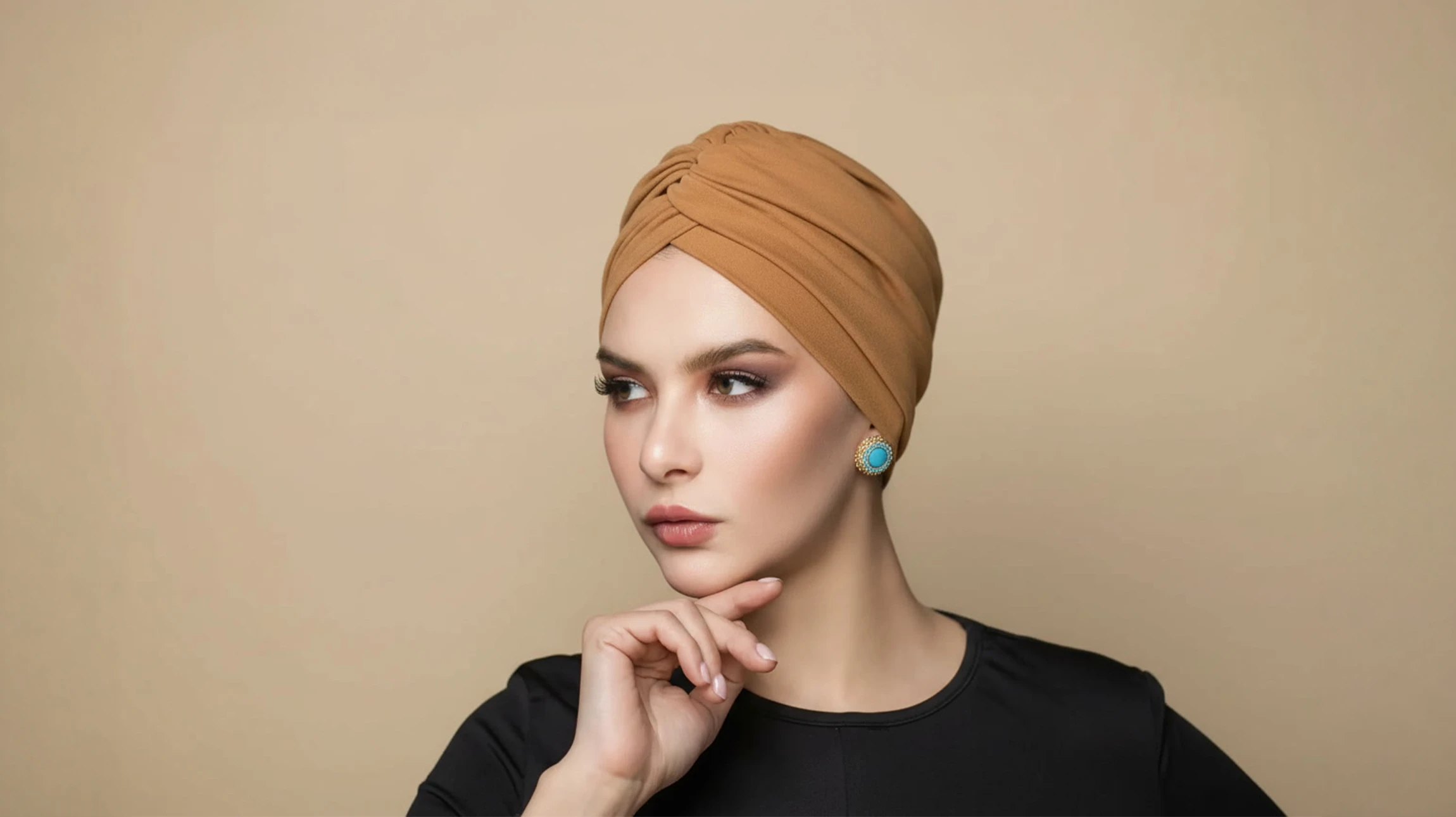 Femme blonde en extérieur portant un turban vert émeraude et lunettes de soleil noires, chemise claire, regard dirigé vers la gauche dans un environnement verdoyant naturel