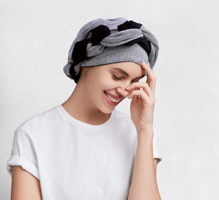 Femme souriante en intérieur portant un bandeau coloré à motifs floraux et un top noir à épaules dénudées