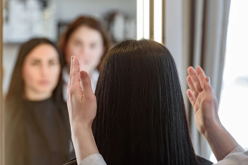 Portrait bienveillant d'une femme en début ou cours de chimiothérapie, assise confortablement dans un cadre intime et chaleureux, portant une perruque naturelle qui lui sied parfaitement. Elle affiche une expression sereine et confiante. À côté d'elle, légèrement floue, une spécialiste en blouse blanche échange un regard rassurant et attentionné, illustrant l'accompagnement humain et l'écoute. L'atmosphère doit véhiculer confiance, dignité et normalité retrouvée. Pas de symboles médicaux agressifs visibles, un environnement lumineux et doux.